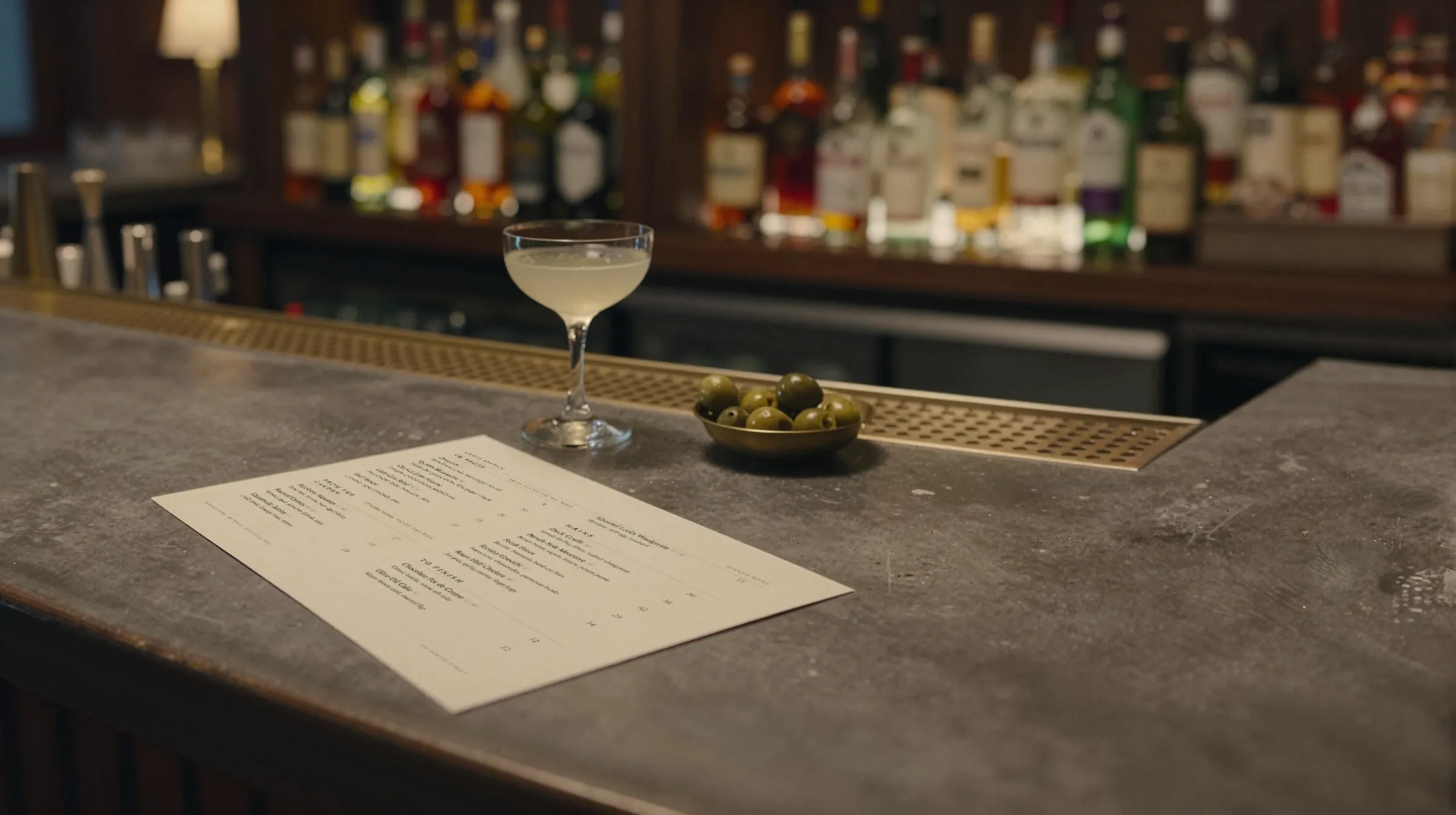 A stone bar counter at night with a glass and a menu