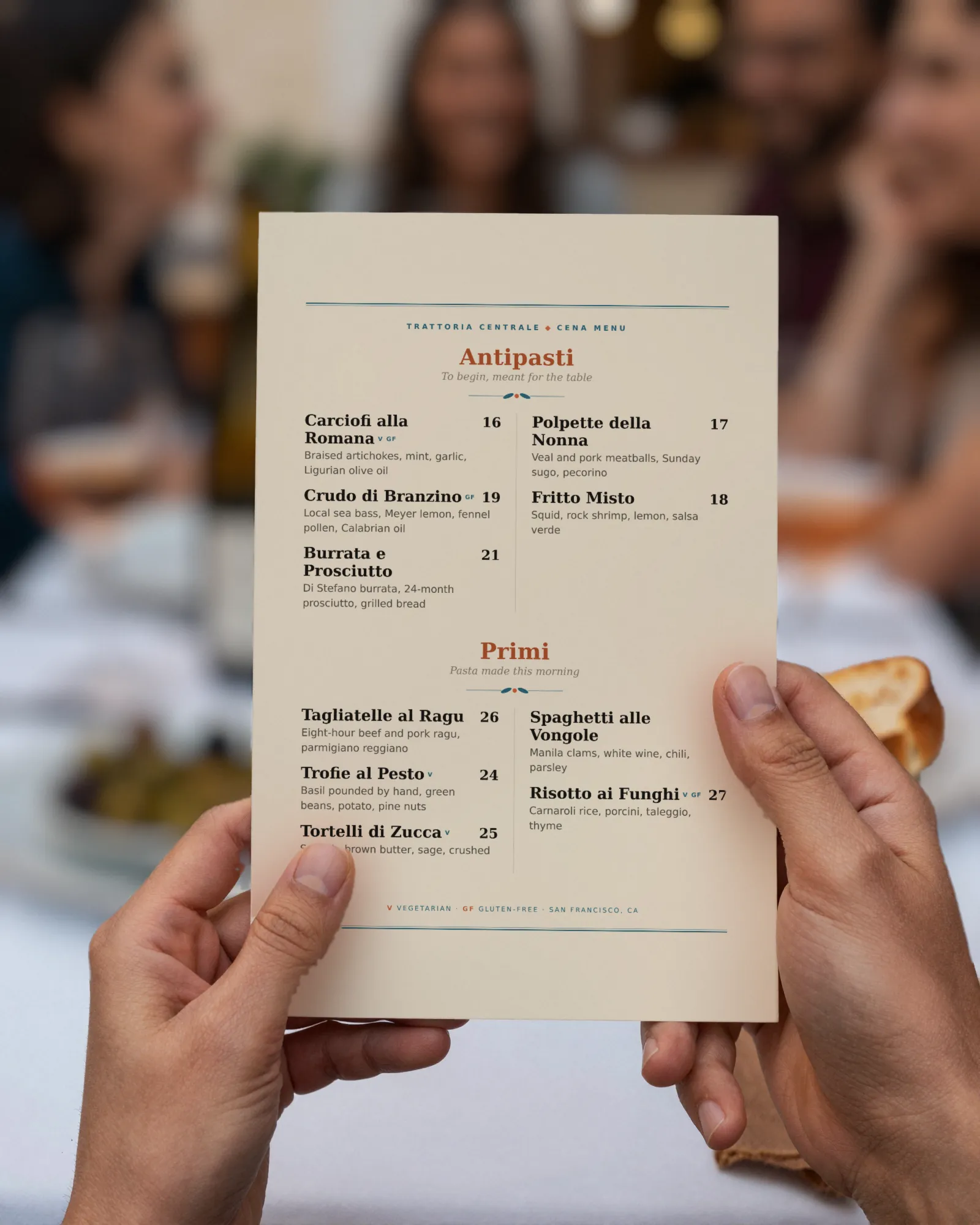 A guest’s hands holding a printed dinner menu at a terrace table with rosé and olives