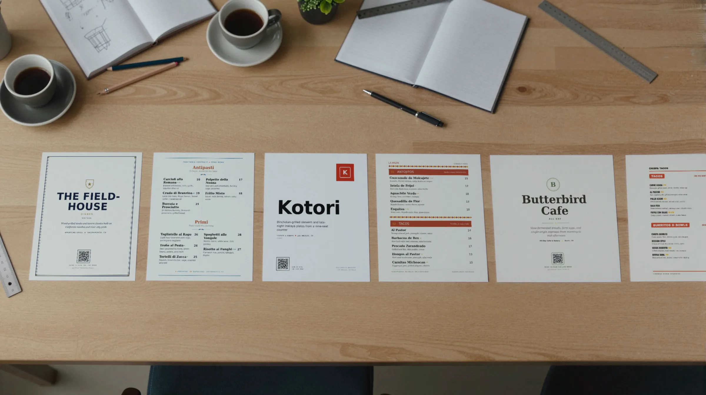 Six printed Gaslamp menu designs laid side by side on a designer’s table with pens and coffee