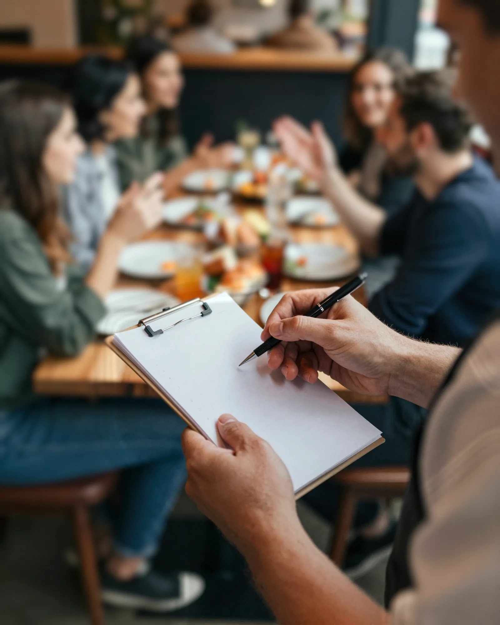 Over a server’s shoulder, a notepad and pen, about to take an order at a busy table