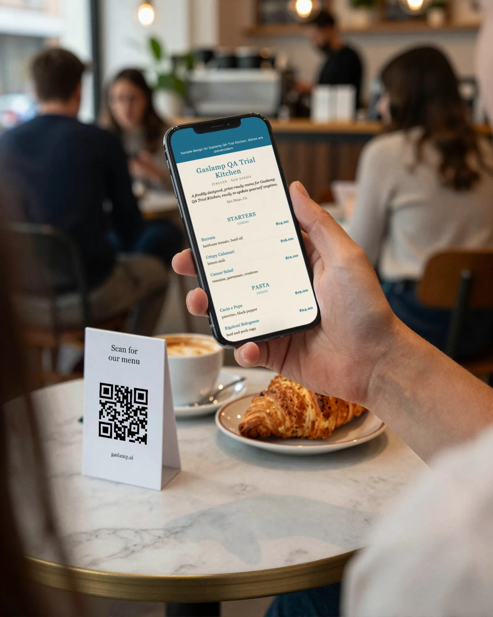 A guest at a cafe table holding a phone that shows a Gaslamp hosted menu, a QR table tent beside the coffee